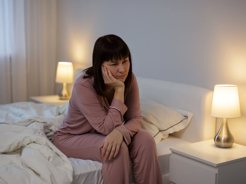 a woman who cant sleep sitting on the side of a bed