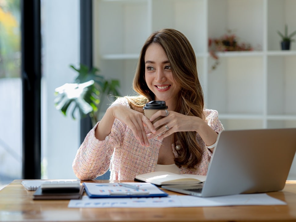 happy woman sitting across her laptop while drinking a cbd infused coffee