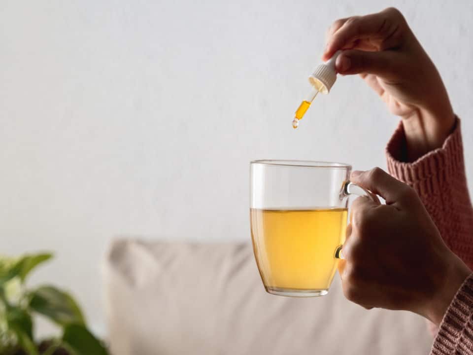 woman holding putting cbd oil in tea cup at home
