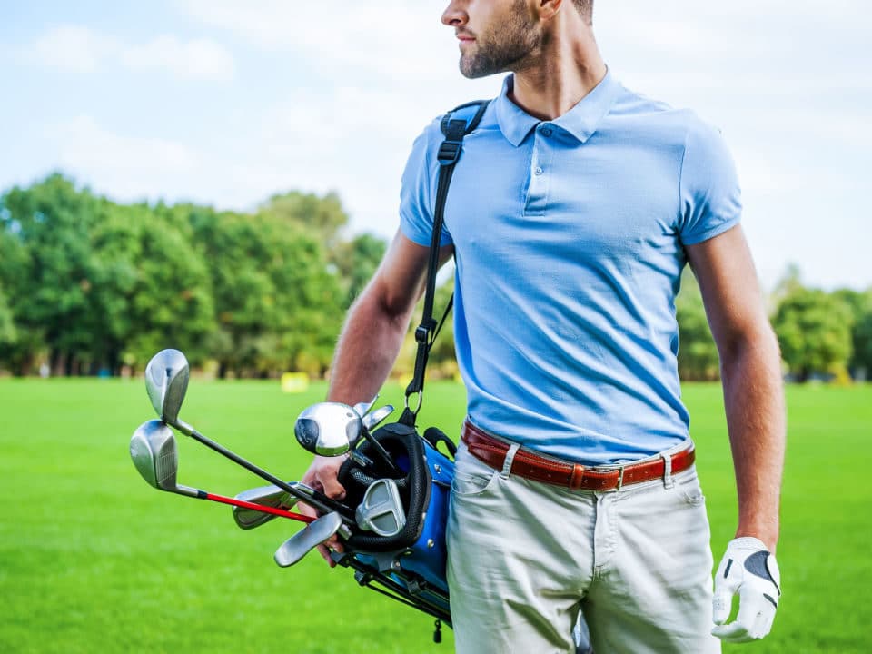 male golfer carrying golf bag while waling on course