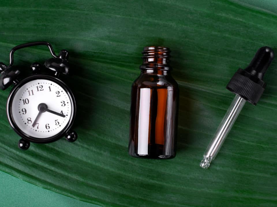 cbd oil and alarm clock on green leaf