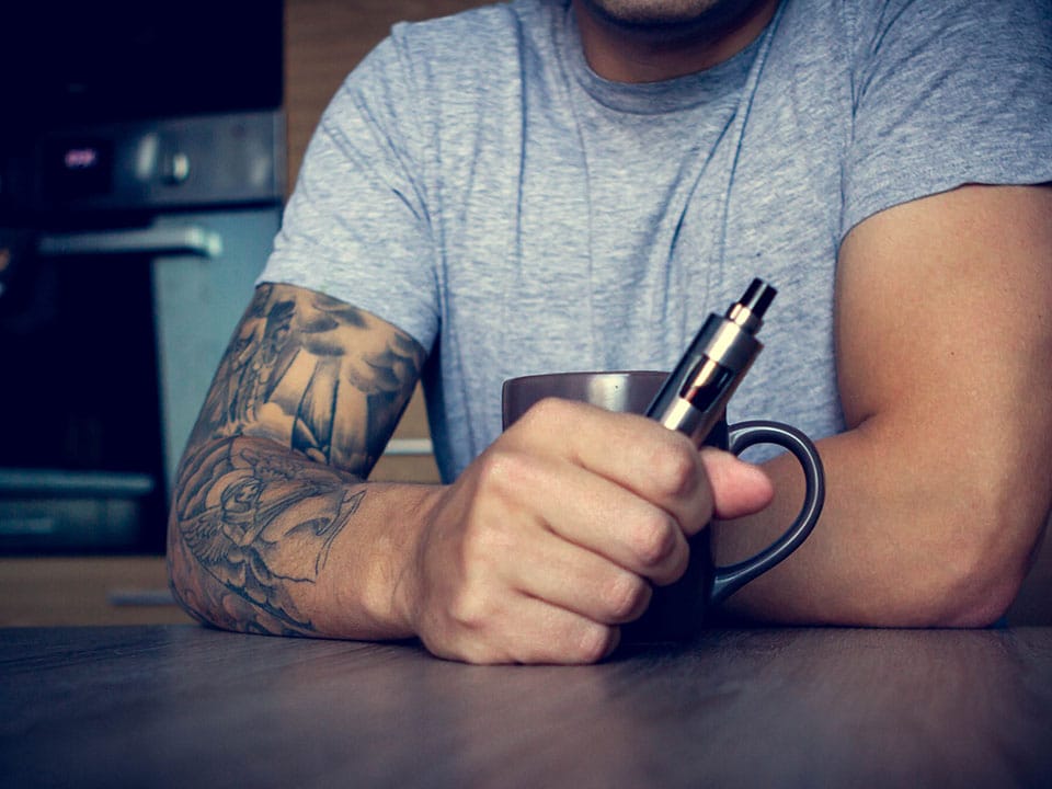 tattooed man smoking cbd vape pen before getting tattoo